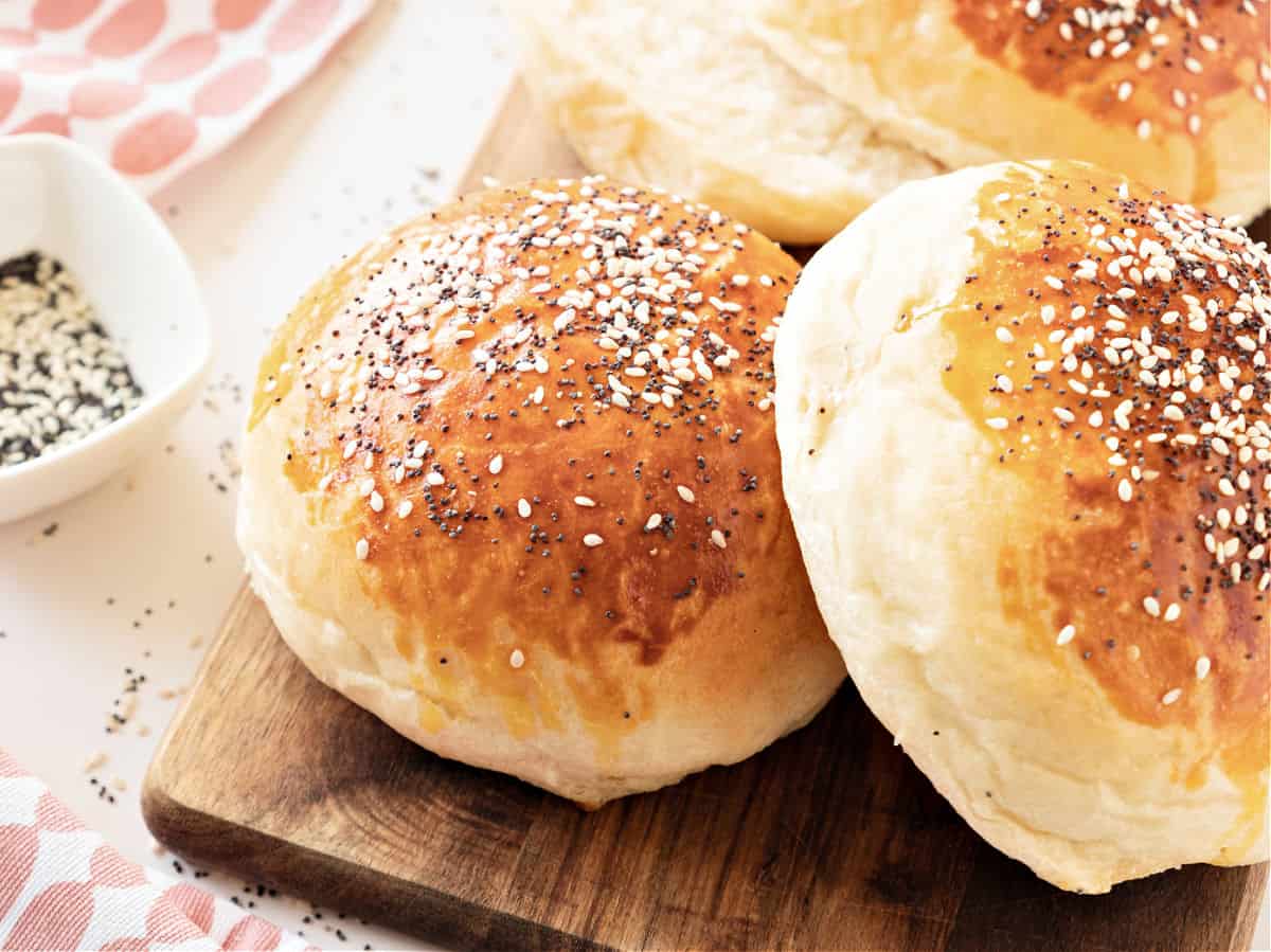 Two hamburger buns with seeds on a wooden board.
