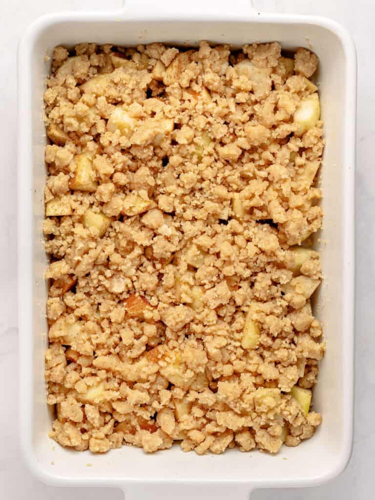 Easy apple crumble in a white dish before baking.