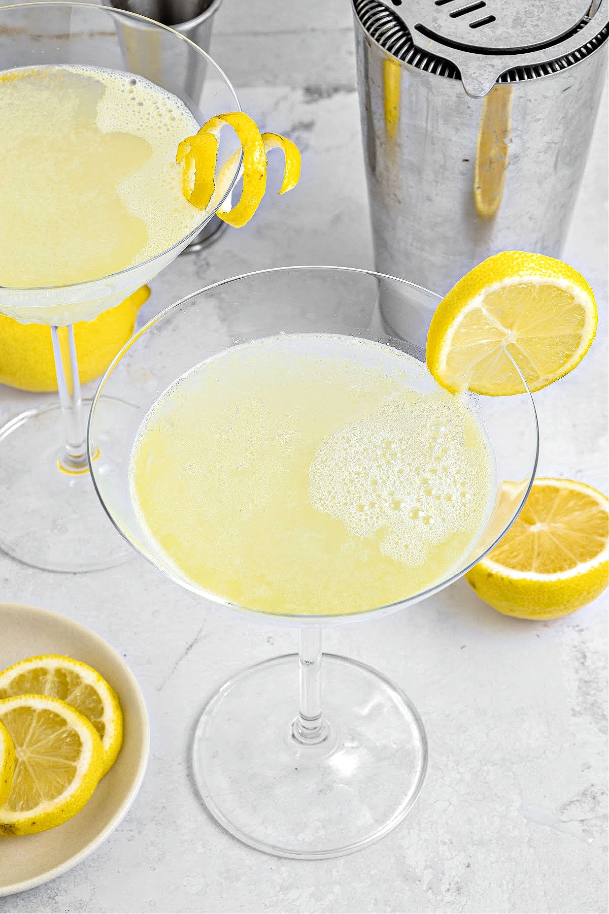 Two lemon martinis. Light gray background, lemon slices, metal shaker.