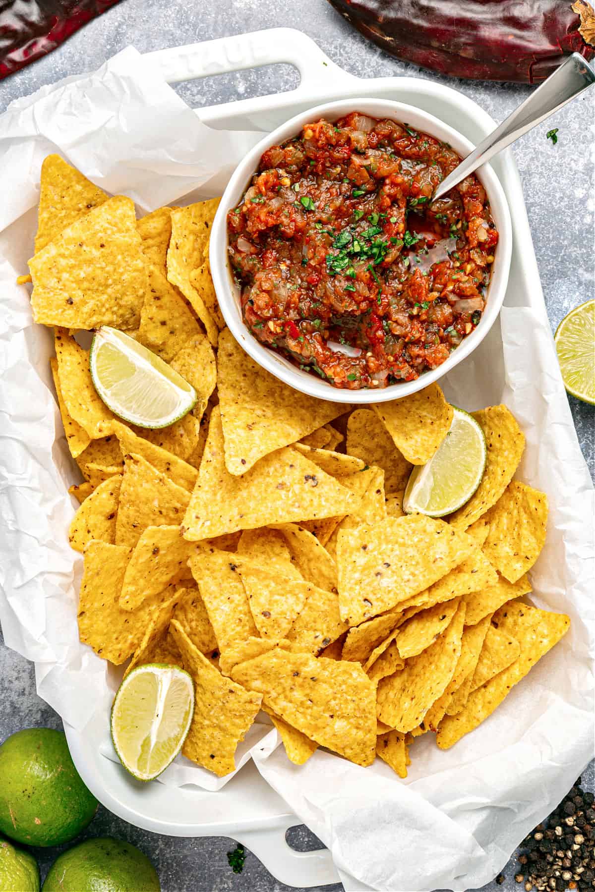 Charred tomato onion salsa with corn chips on a white tray. Lime wedges.