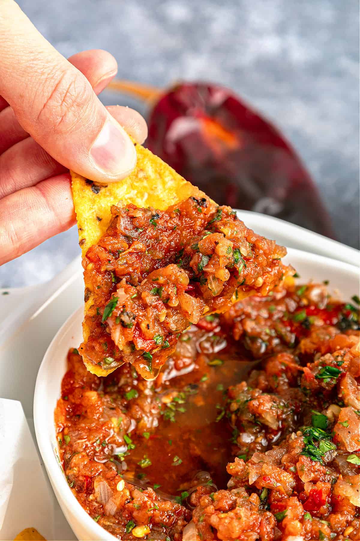 Holding a corn chip with salsa ranchera. White bowl, gray background.