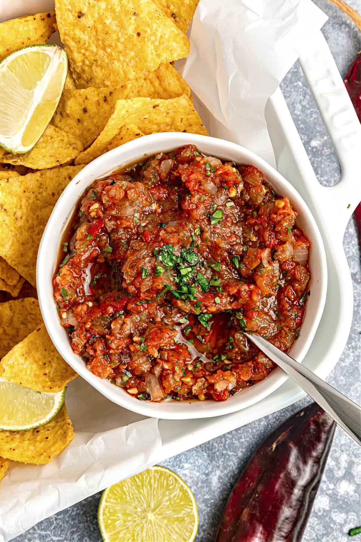 Tomato salsa in white bowl with corn chips on a white tray.