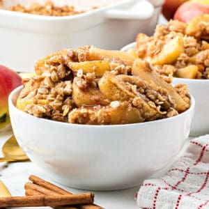 White bowls with apple crumble. Cinnamon sticks, red checkered towel.