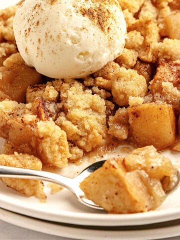 Old fashioned apple crumble served on a white plate with scoop of ice cream.