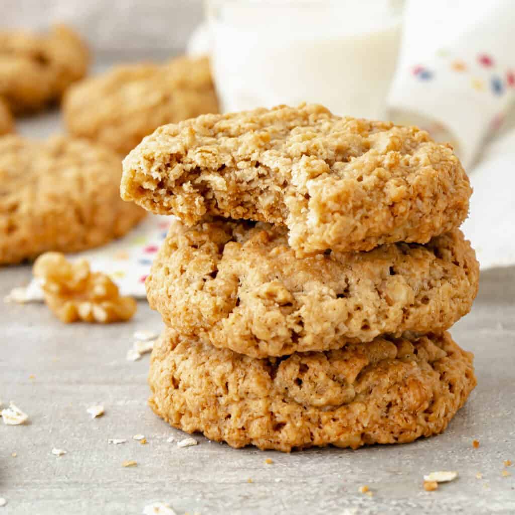 Stack of three oat cookies, top one is bitten. Gray surface.