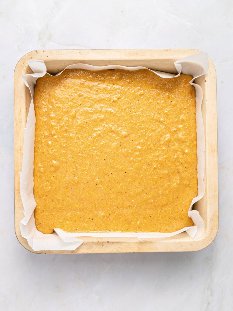 Parchment-lined square pan with sweet potato cornbread batter.