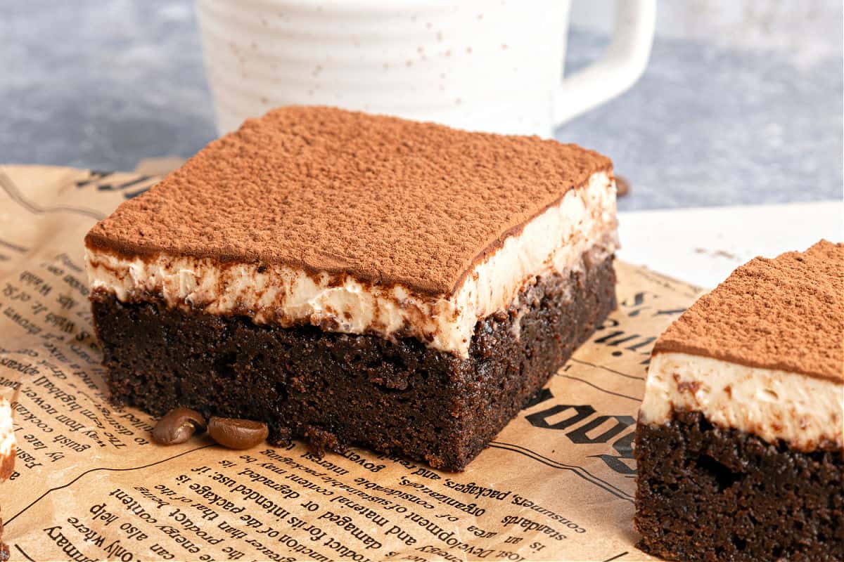 Squares of tiramisu brownies on yellowish newspaper sheet. Gray background.