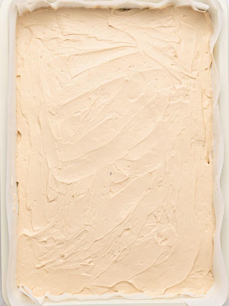 Tiramisu mixture topped brownies in a rectangular, paper-lined pan.
