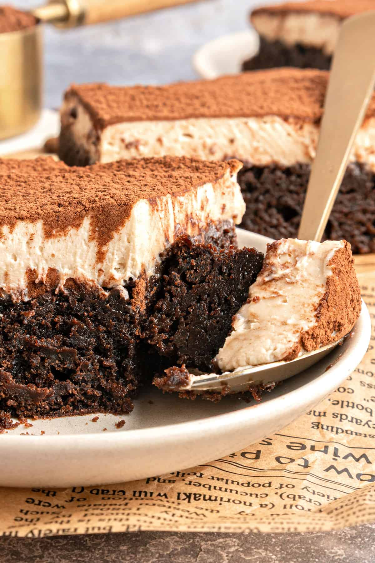 Spoon and plate with tiramisu brownie serving. Newspaper surface.