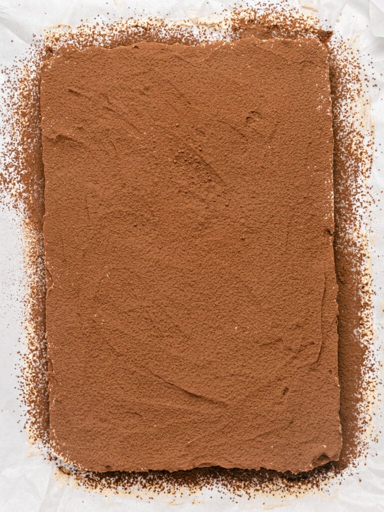 Cocoa-dusted tiramisu brownies block before cutting on parchment paper.