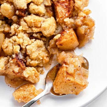 Serving of apple crumble on a white plate with a spoon.