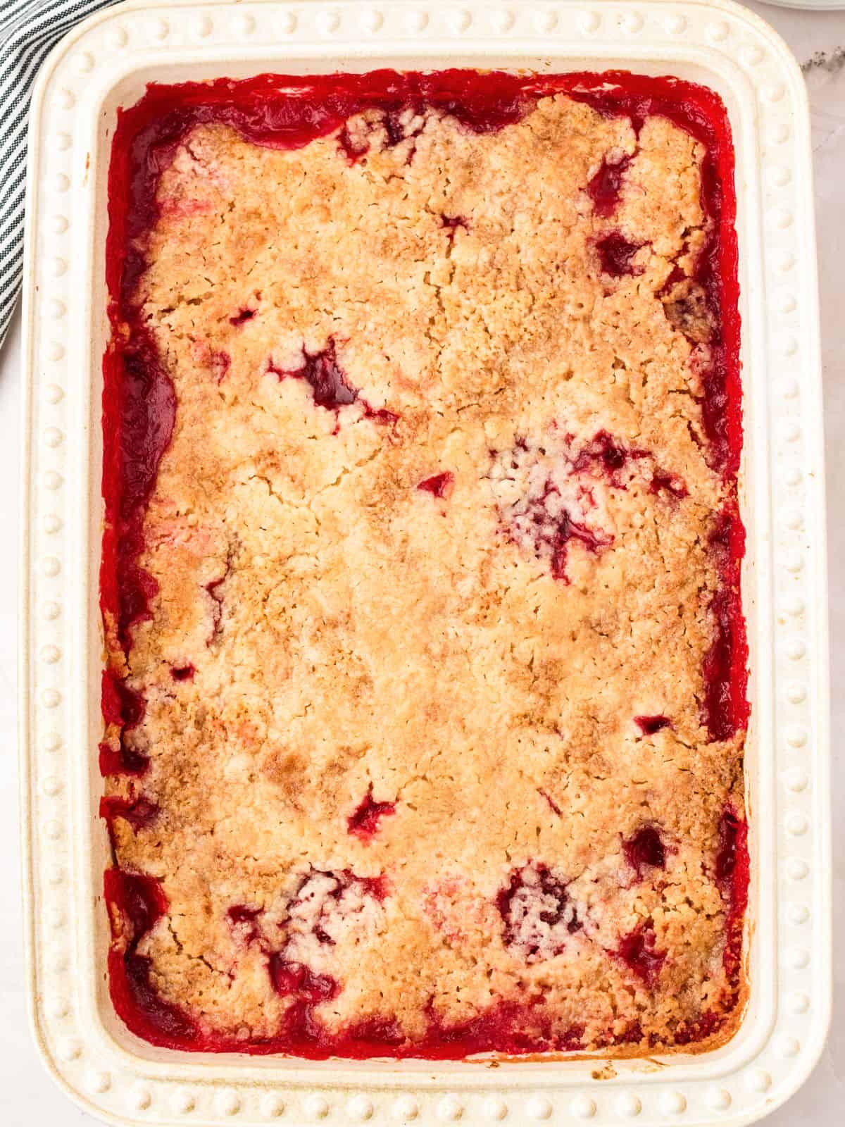 Baked strawberry and pineapple dump cobbler in a cream-colored dish.