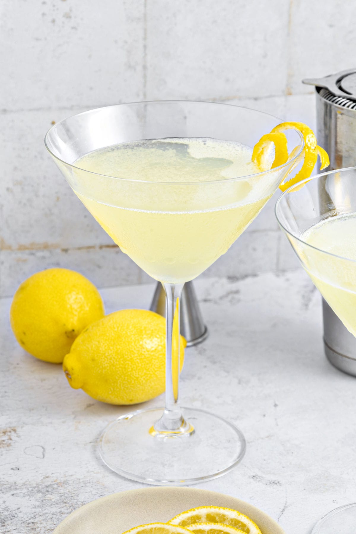 Limoncello martini in a classic glass. Whole lemons, light gray background.