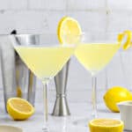 Stem glasses with limoncello martini. Gray background, shaker, lemon slices.