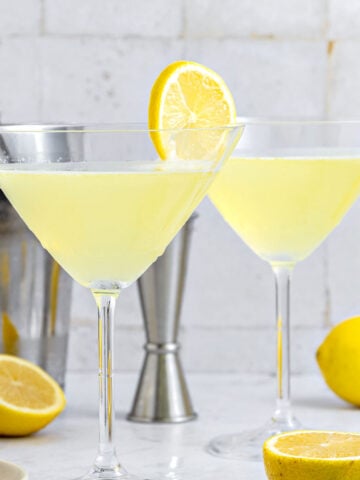 Stem glasses with limoncello martini. Gray background, shaker, lemon slices.