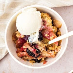White bowl of apple blackberry crumble with ice cream. Beige background.