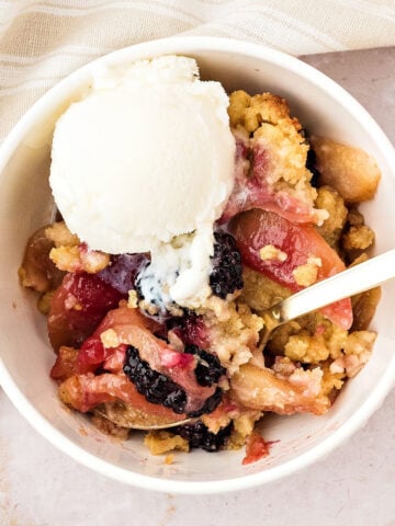 White bowl of apple blackberry crumble with ice cream. Beige background.