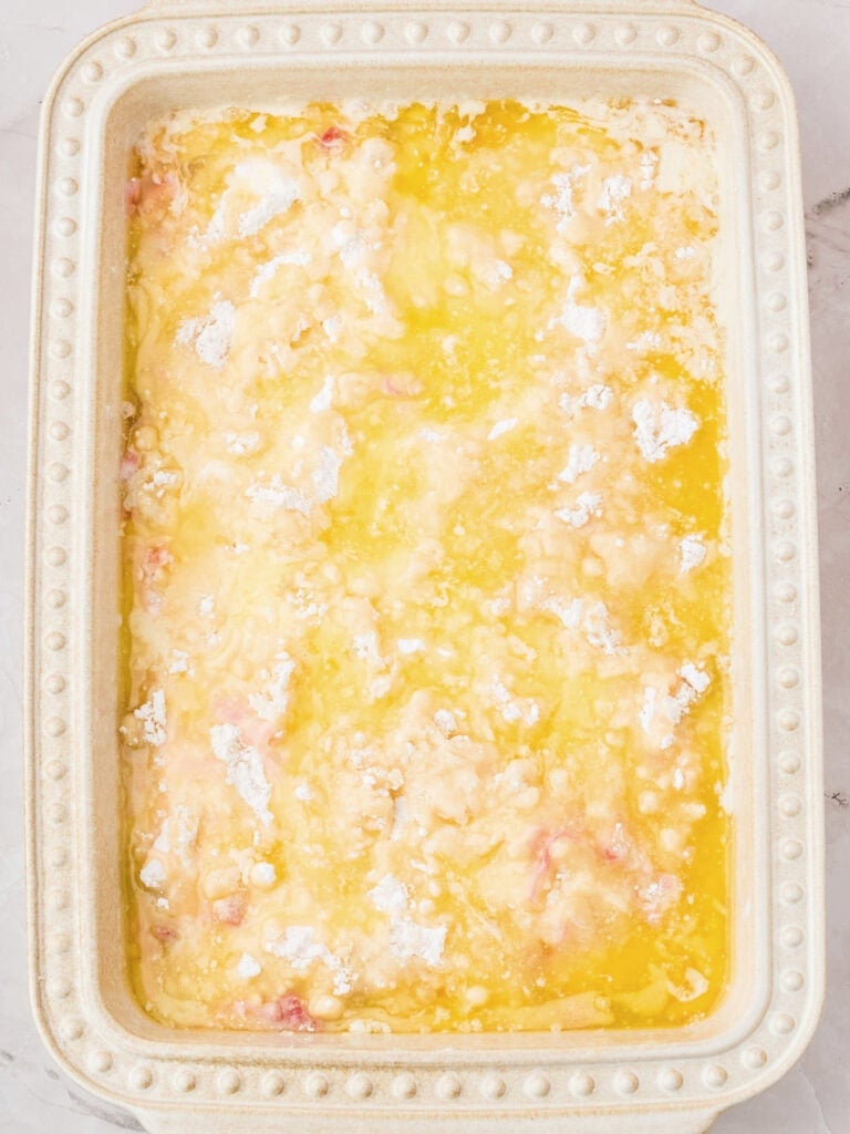 Melted butter over cake mix in a cream-colored baking dish.