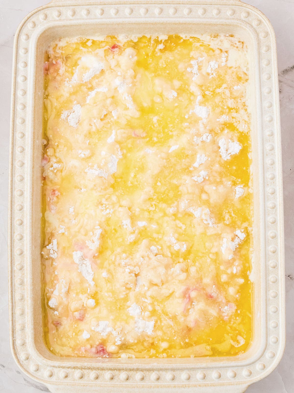 Melted butter over cake mix in a cream-colored baking dish.