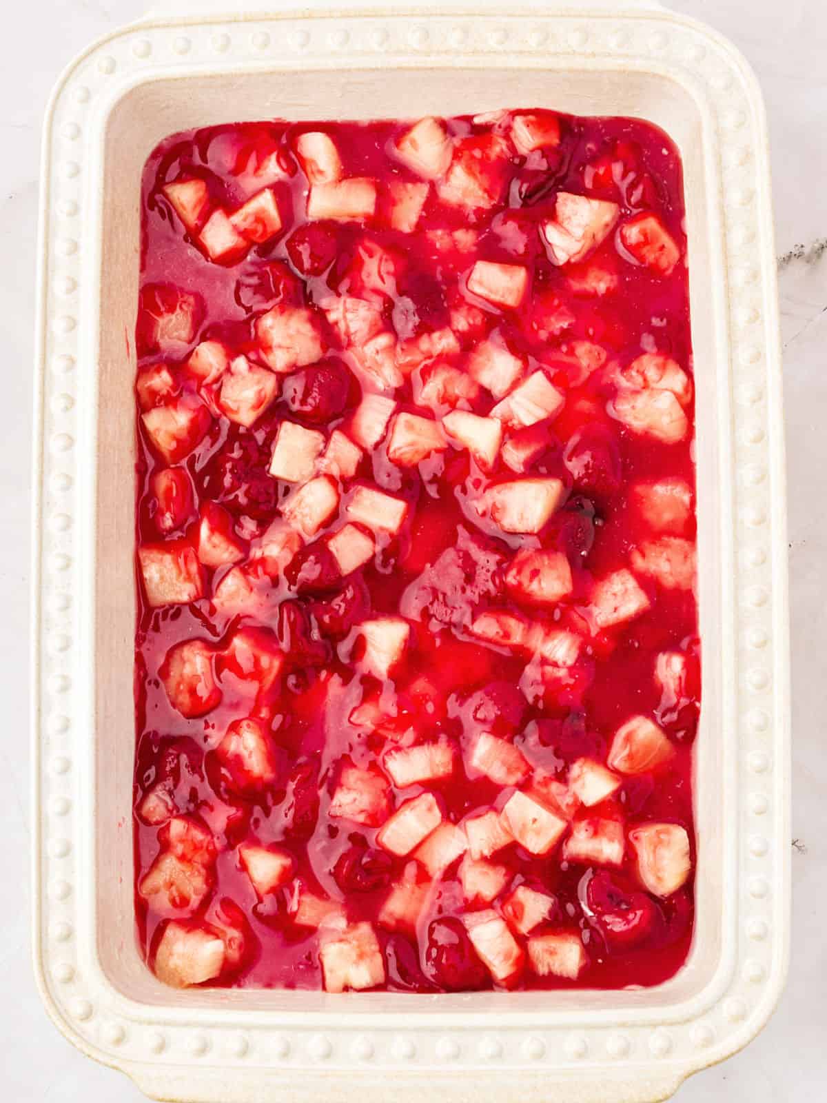 Filling for pineapple strawberry dump cake in a cream-colored baking dish.