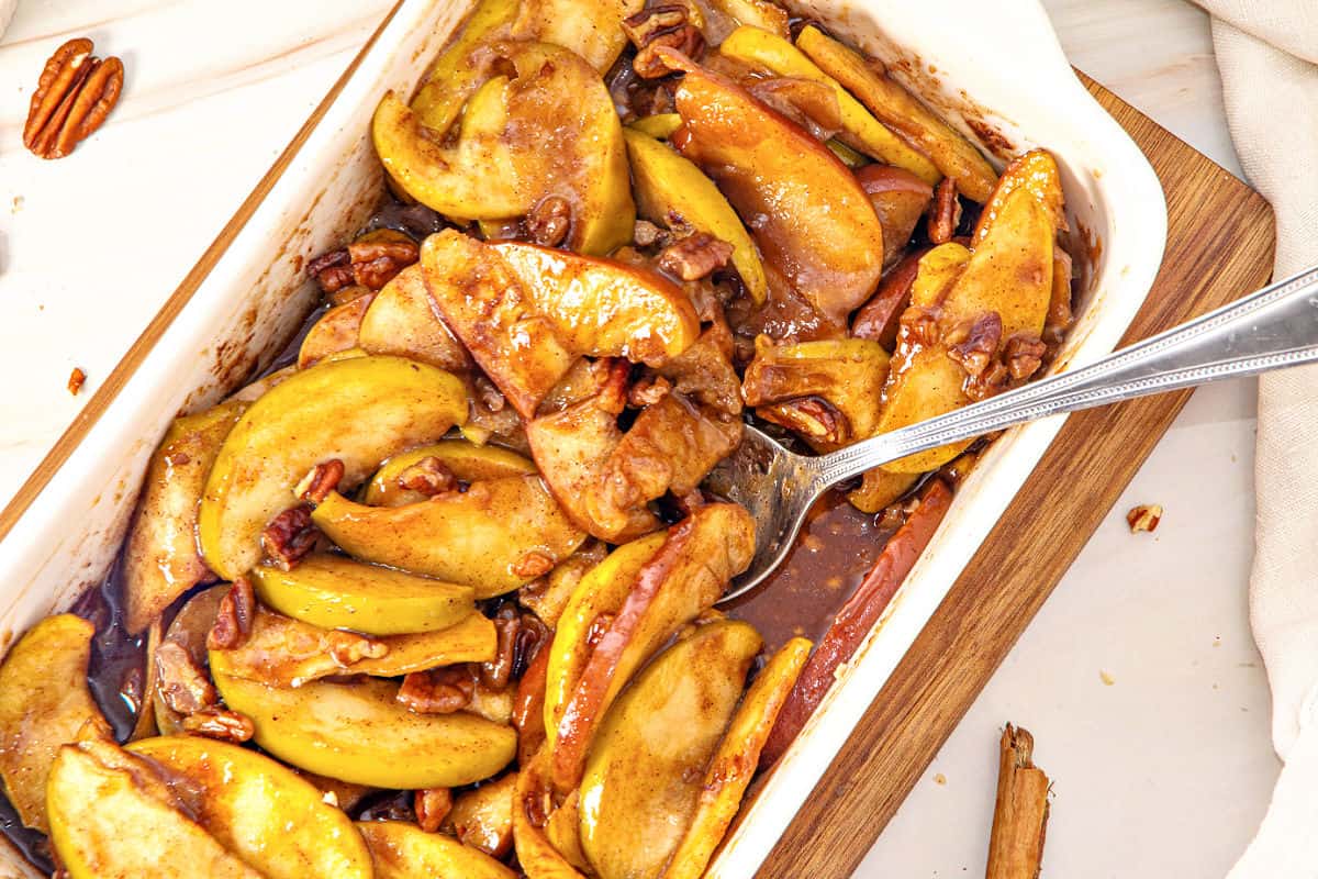 Partial view of white rectangular dish with baked apples in syrup.