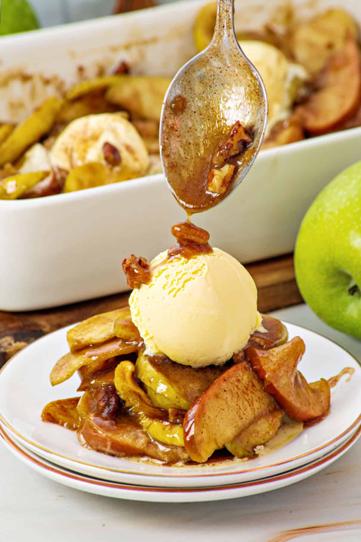 White plate with serving of apple cinnamon slices in syrup. Ice cream on top. Dish in the background.