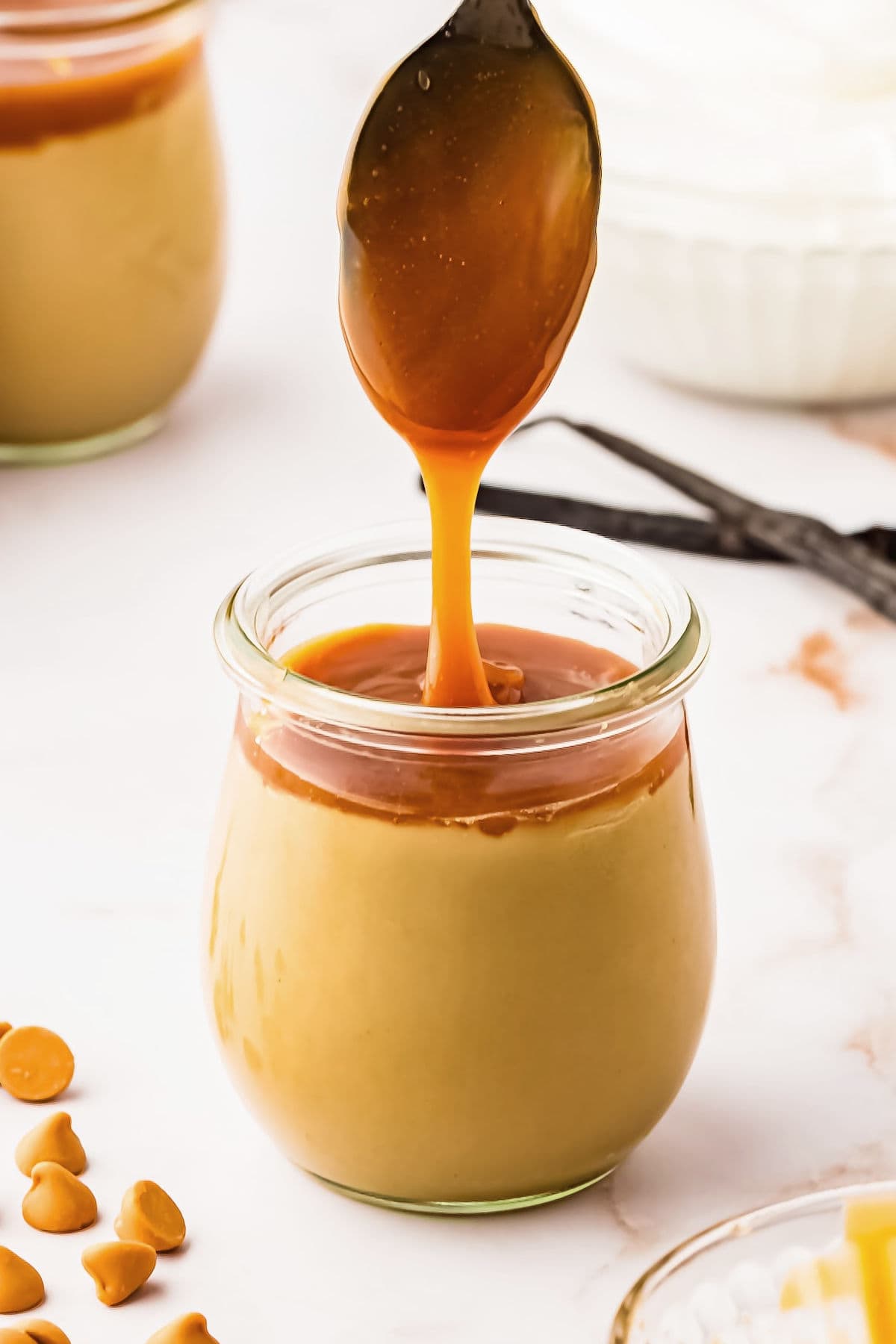 Spooning caramel sauce on jar of butterscotch pudding. White background.