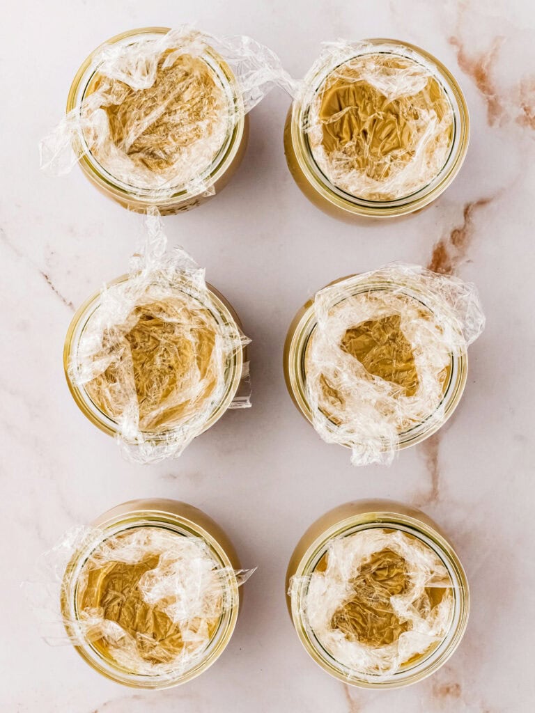 Plastic wrap topped jars of butterscotch puddings. Marbled background.