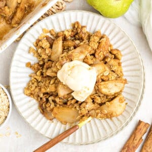 Fluted white plate with serving of pear crumble with oats and ice cream. Wooden fork.
