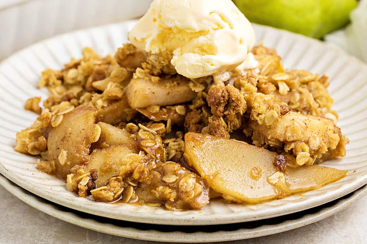 Ice cream topped pear oat crisp serving on a white plate.