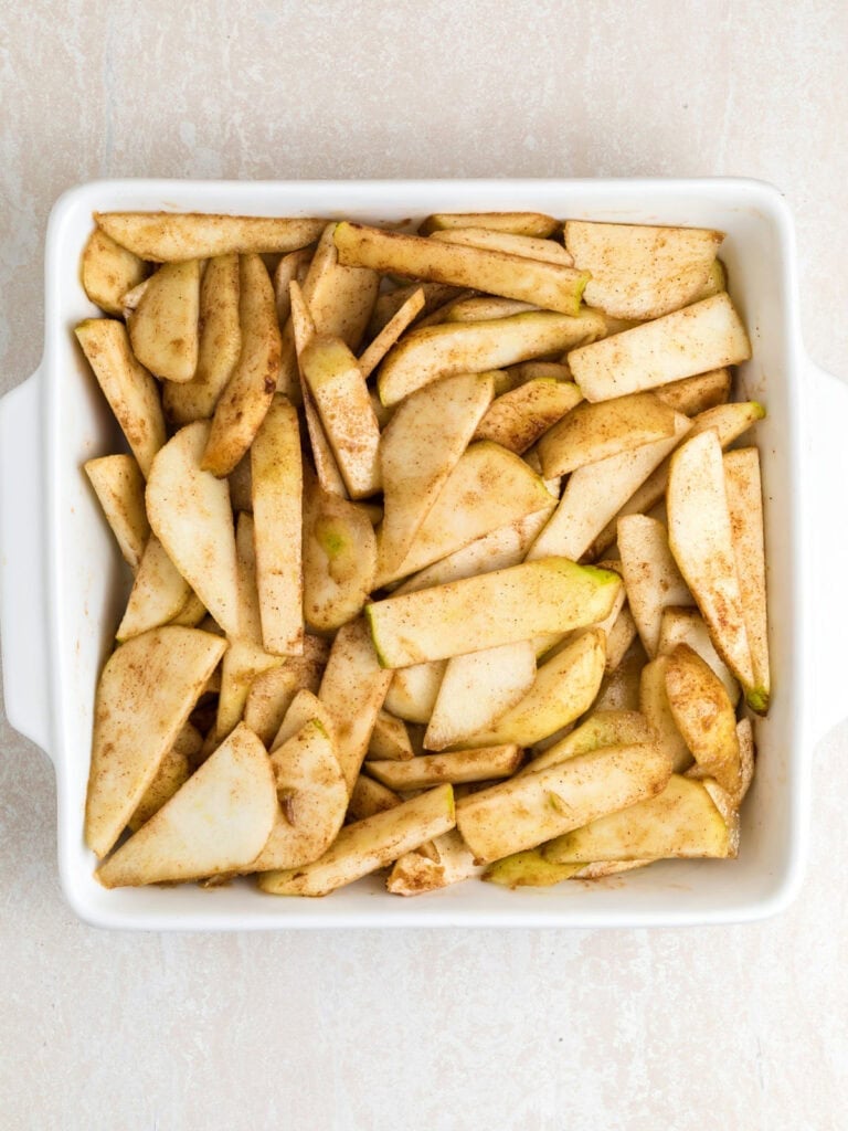 Slices of pears with spices on a square white ceramic dish. Light gray background.