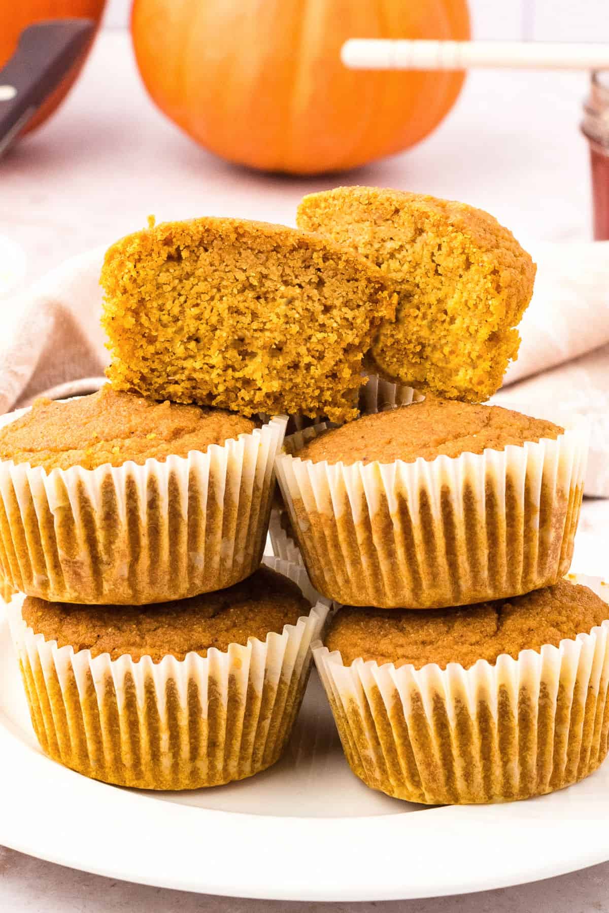 Stacked whole and halved pumpkin cornbread muffins in paper liners. White plate.