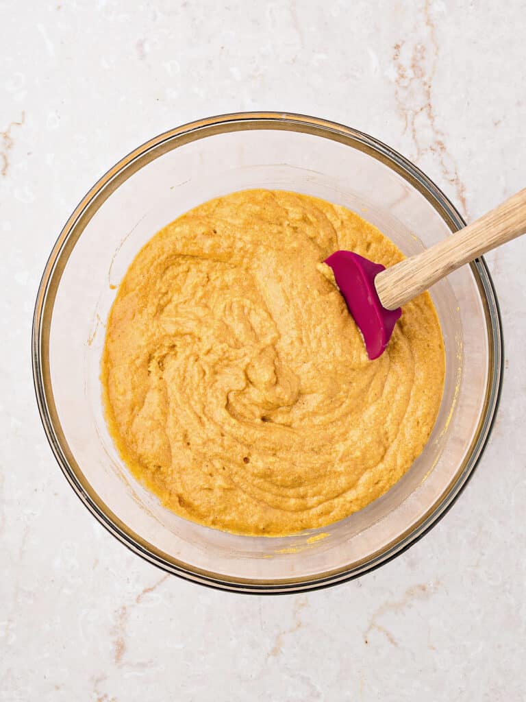 Batter for pumpkin corn muffins in a glass bowl. A spatula. Marbled surface.