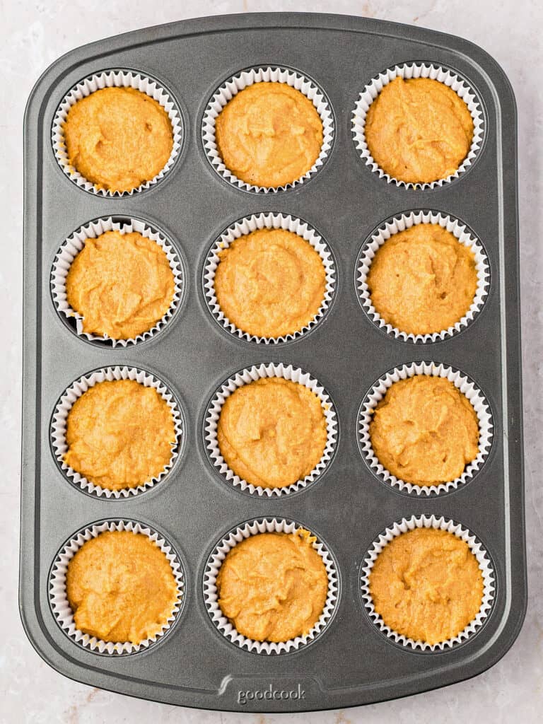 Dark gray muffin pan with pumpkin cornbread muffin batter. 