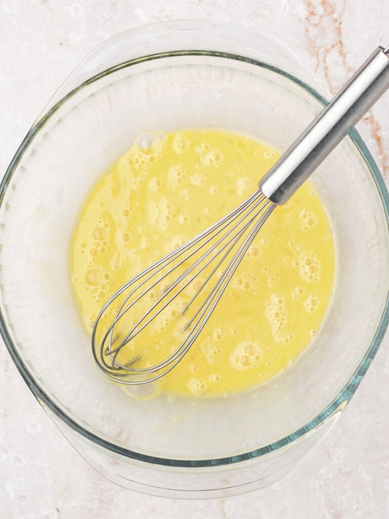 Glass bowl with beaten eggs and sugar. Metal whisk.