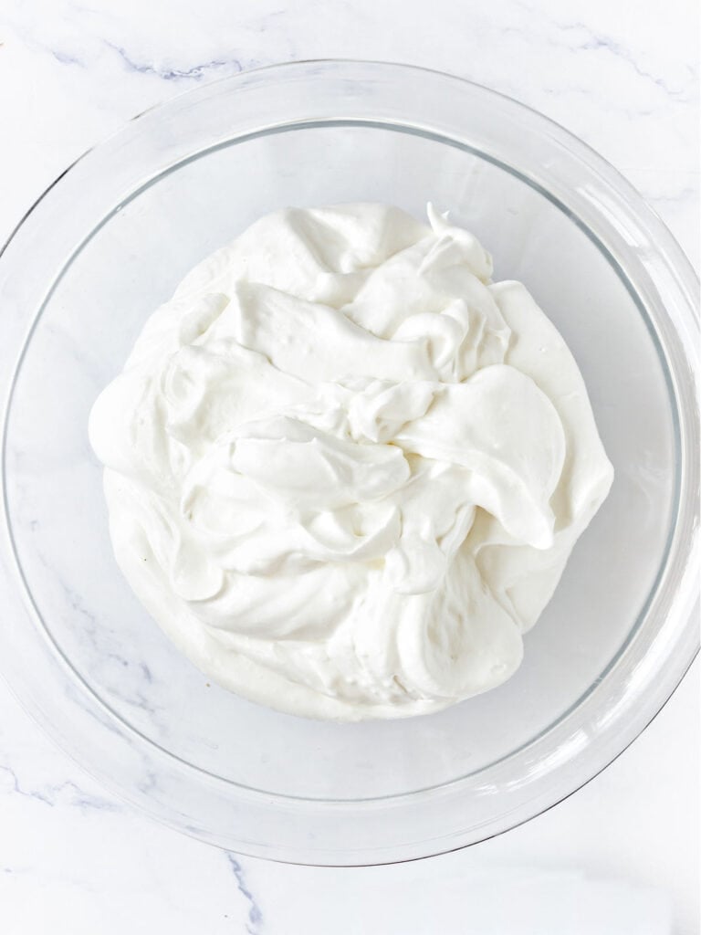 Thick whipped cream in a glass bowl. White surface.