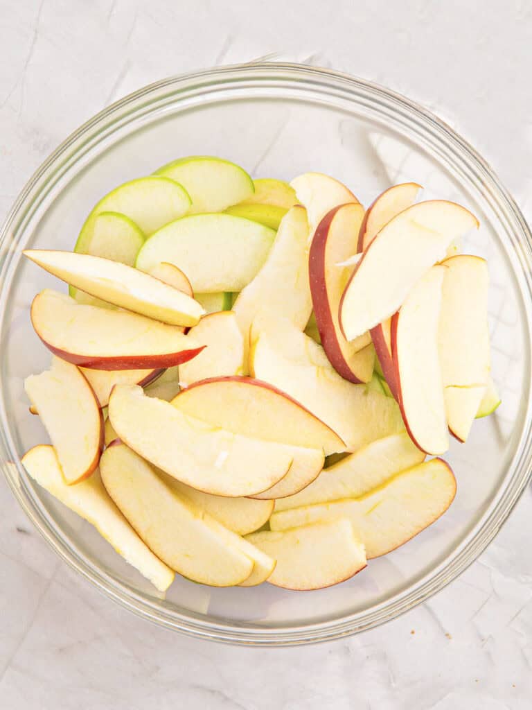Raw, unpeeled apple slices in a glass bowl.