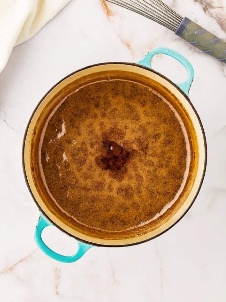 Dark caramel in a saucepan with blue handles. White marble background. Top view.