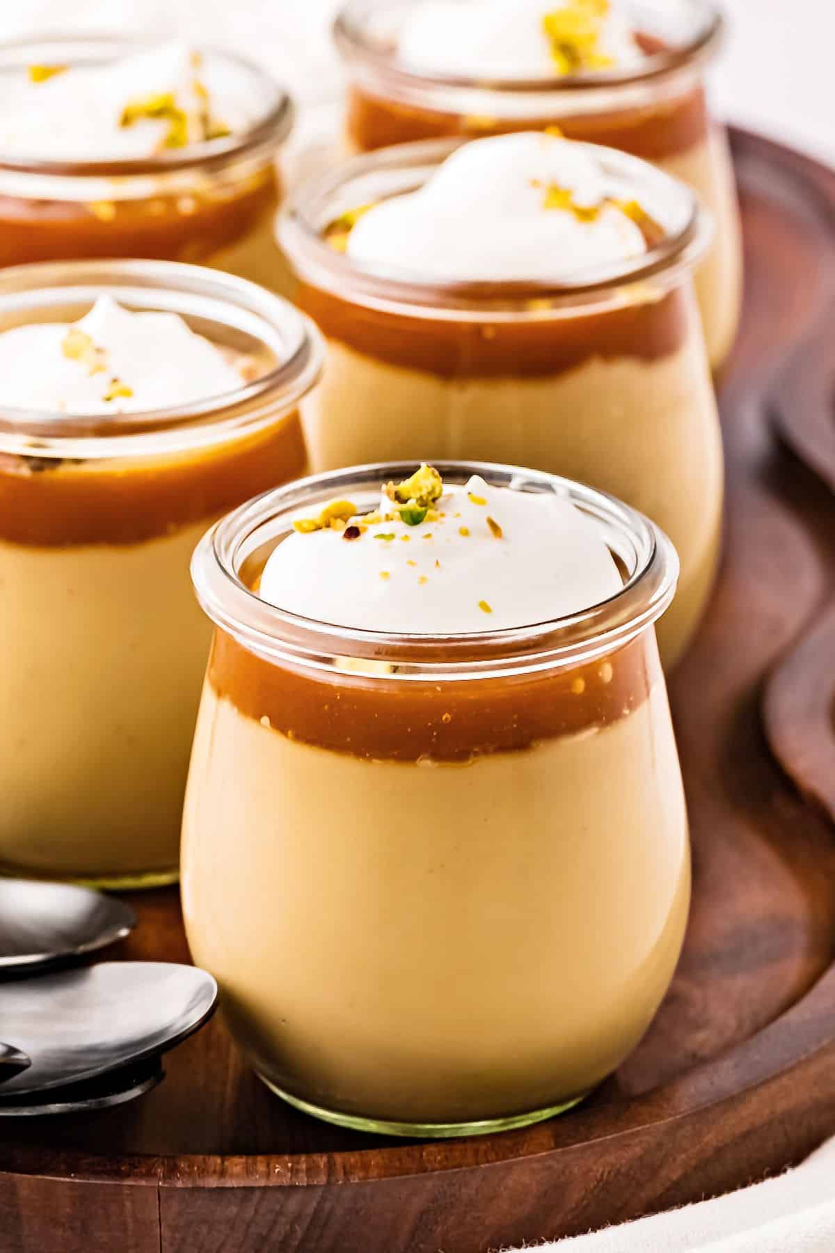 Several jars of butterscotch cream pudding on a wooden tray.
