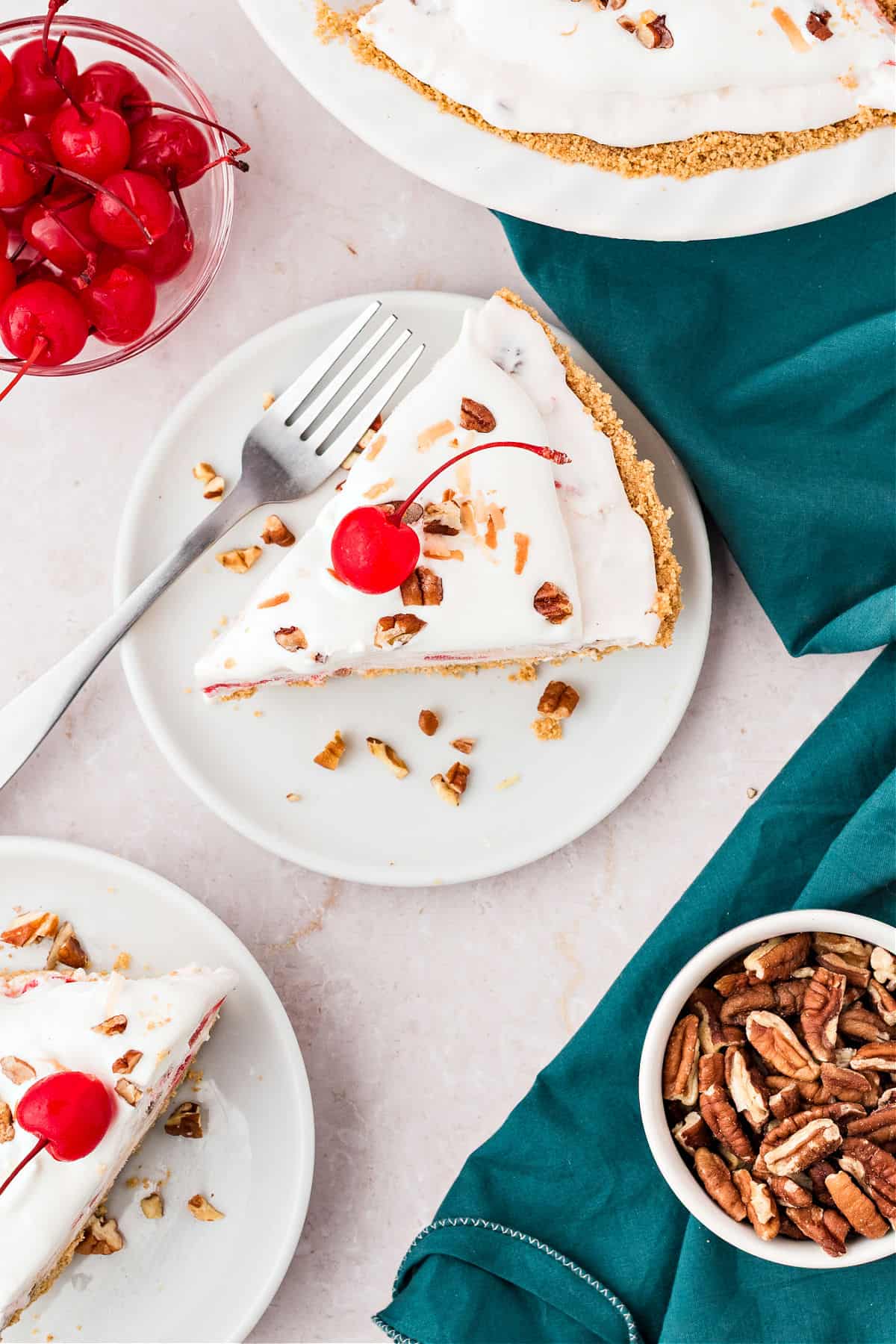 Teal and white background with white plates of millionaire pie servings. Cherry and pecan bowls.