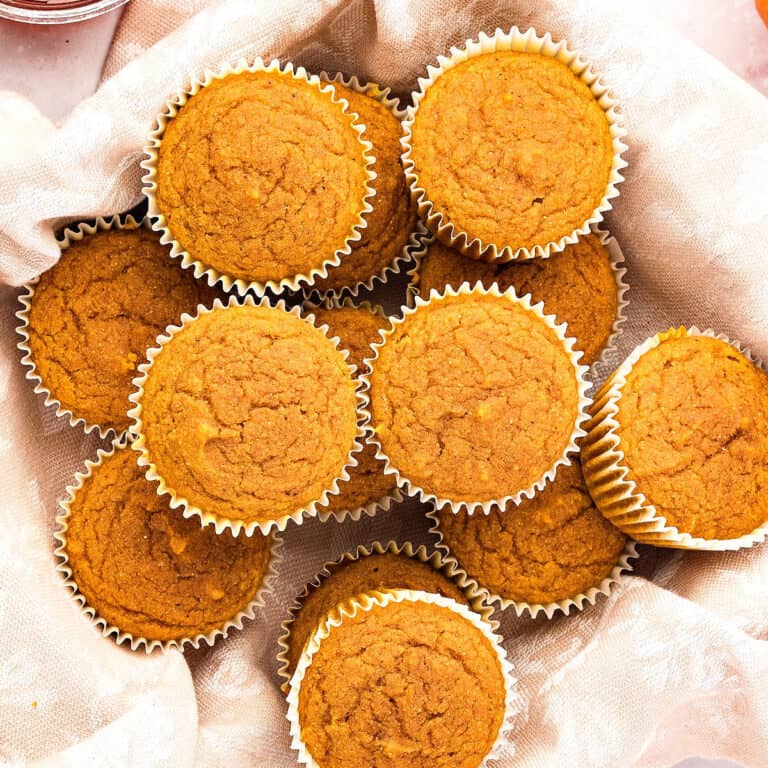 Several pumpkin cornbread muffins piled on a white brocate cloth.