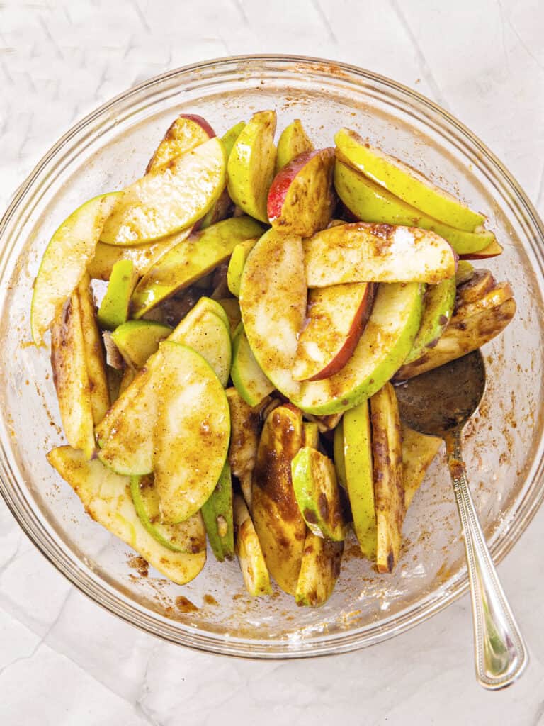 Unpeeled apple slices in a glass bowl with spices and flour.