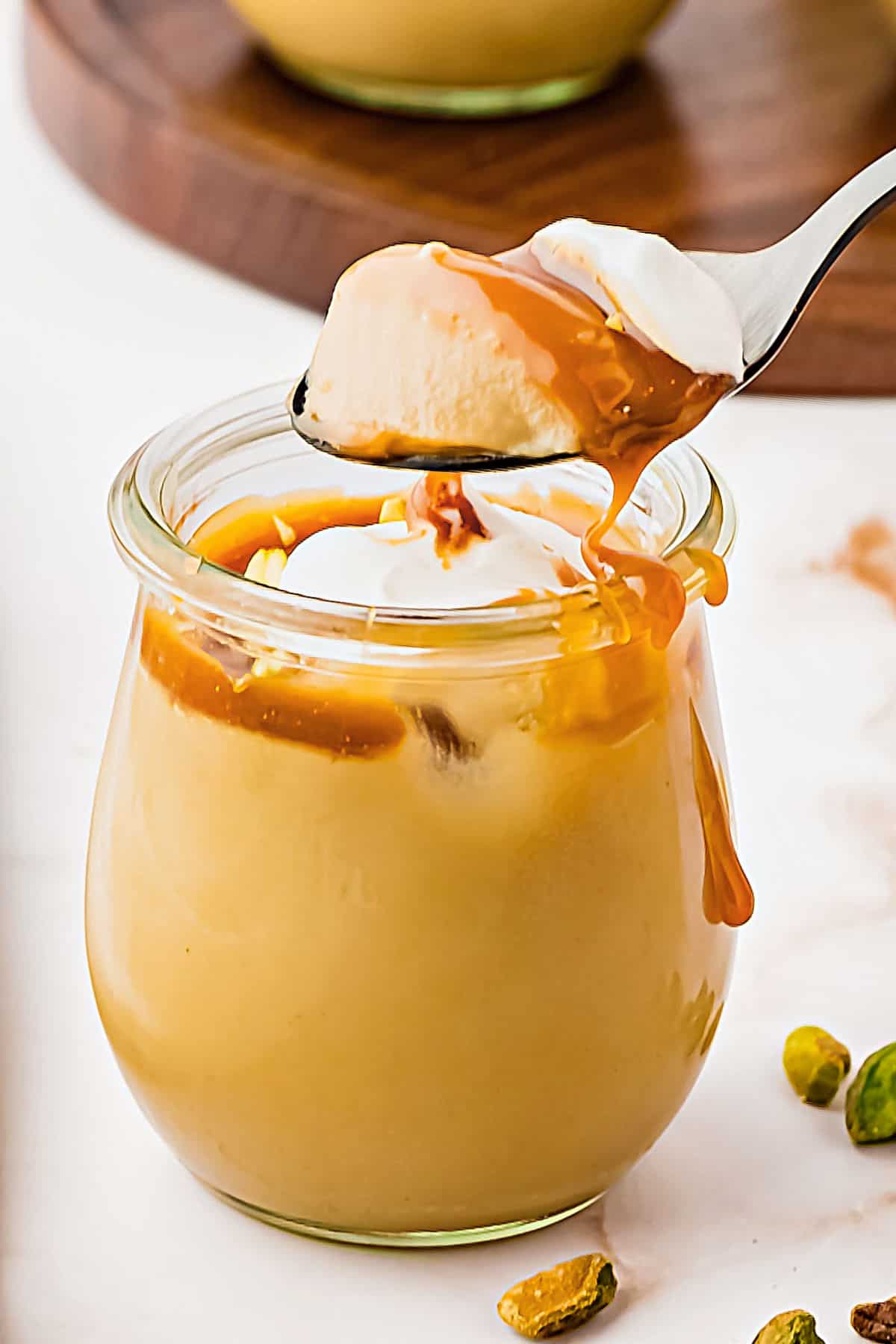 Spoon with bite of butterscotch pudding over jar. White surface.