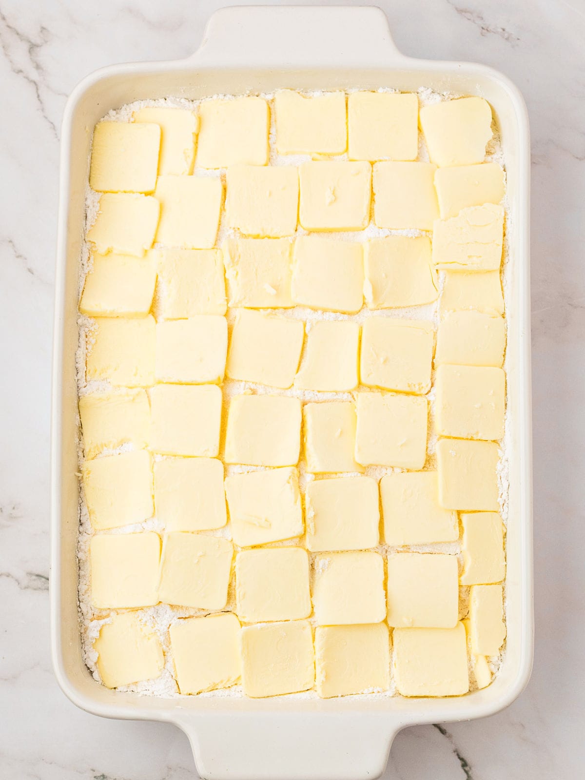 Sliced butter pieces over cake mix in a white baking dish.