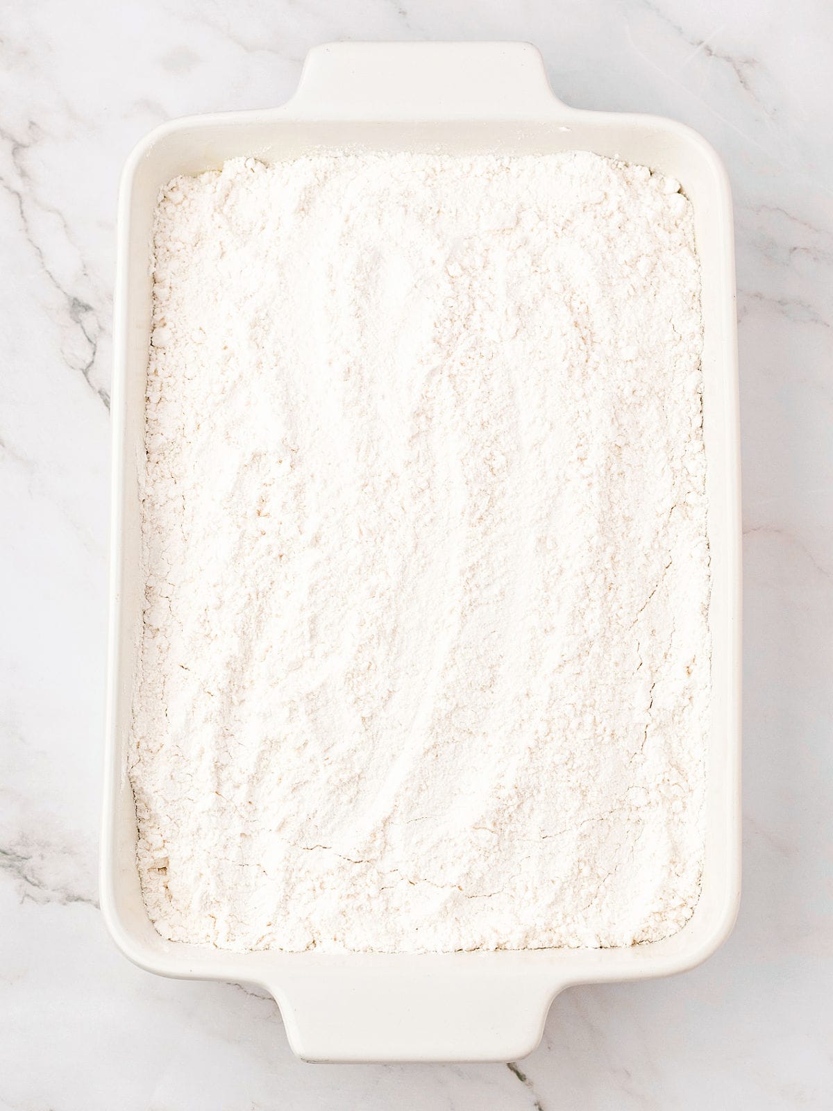 White baking dish with cake mix topping. White marbled background.