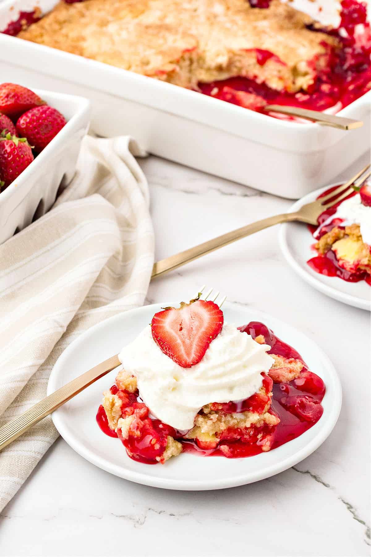 Ceramic white dish and plates with strawberry dump cake. Gold forks.