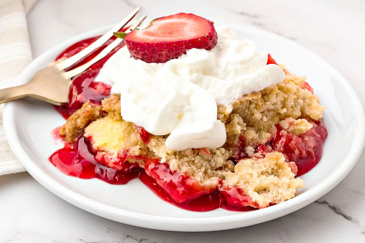 Close up white plate with serving of cream-topped strawberry dump cake.