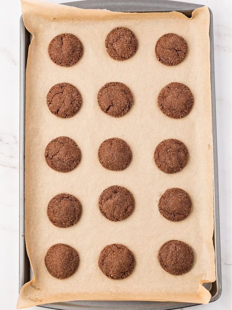 Baked sugar-coated chocolate cookies on a parchment-lined sheet.