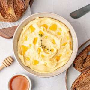 Whitish bowl with whipped honey butter. White background. Honey bowl and dipper. Bread.