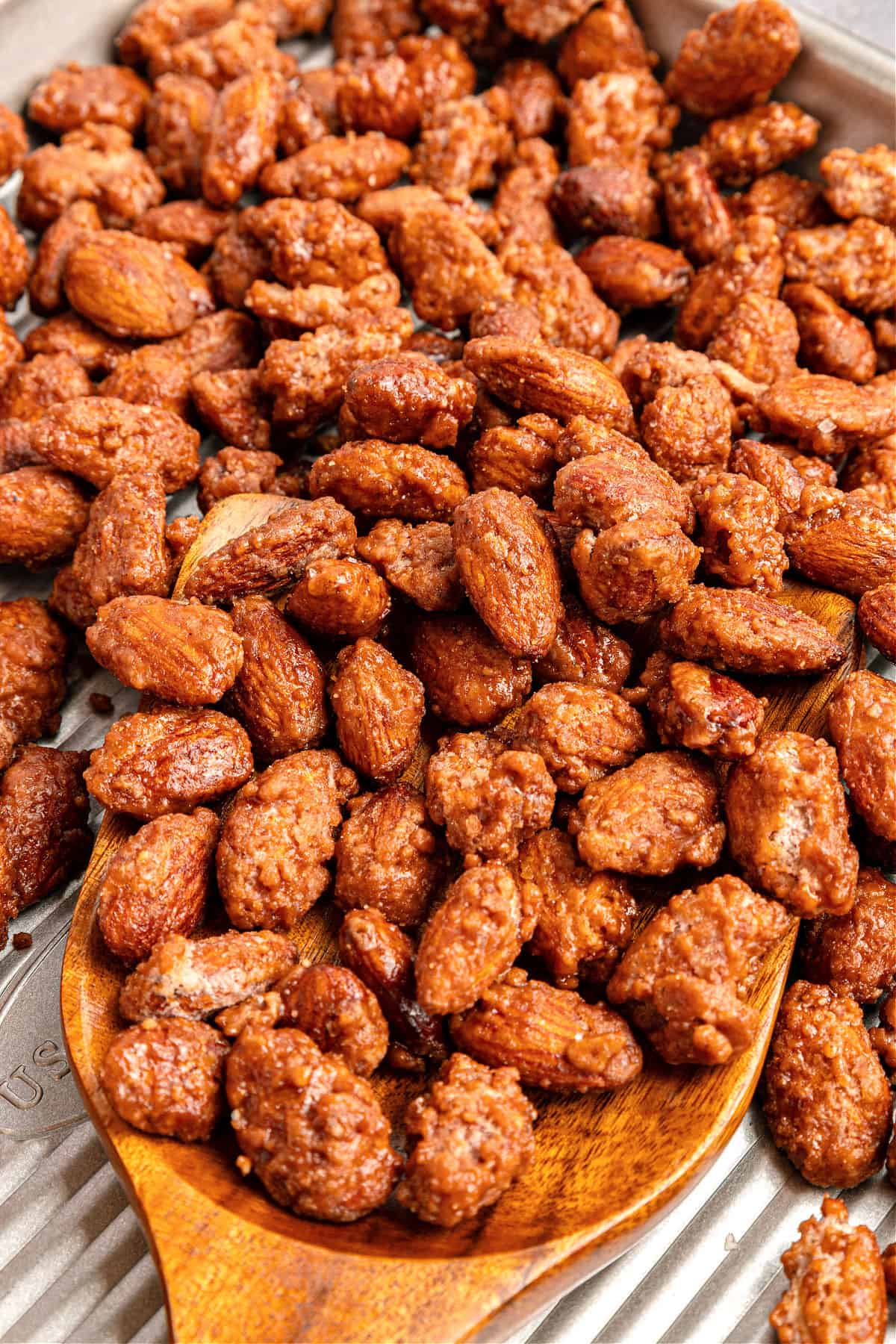 Wooden spoon of candied almonds on a metal tray.